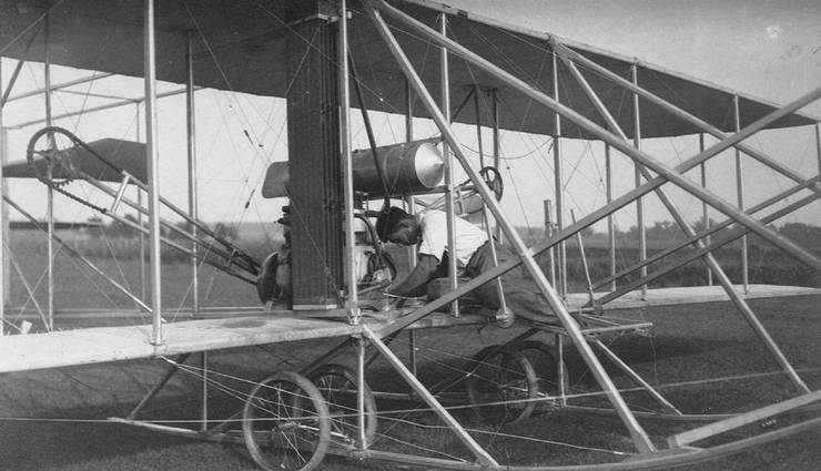 Unidentified aviator working on Wright transitional aircraft, possibly tending to magneto control.