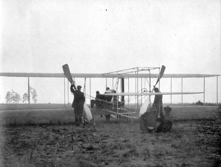 Preparing to launch a Model B, two men stand ready to pull the propellers through, two hold the tail boom, Coffyn stands at the front, tending to the engine, and one is seated on board.